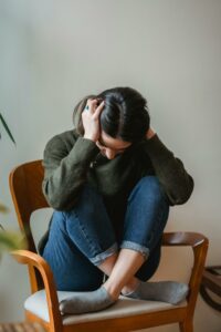 Jeune femme assise sur une chaise, tenant sa tête entre ses mains, signe de mal-être