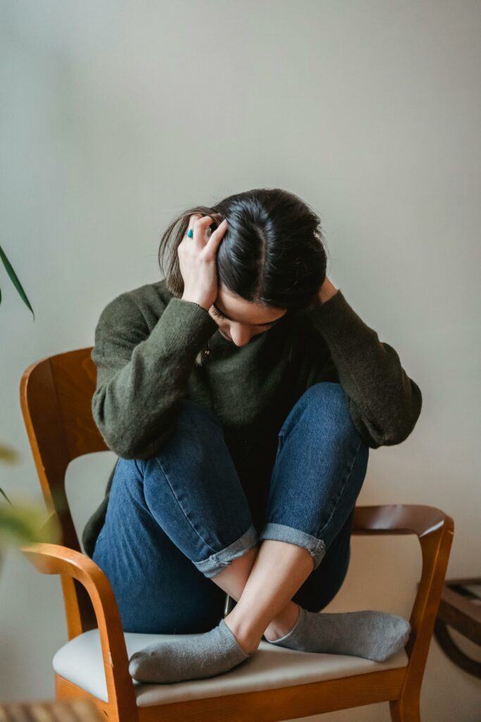 Jeune femme assise sur une chaise, tenant sa tête entre ses mains, signe de mal-être