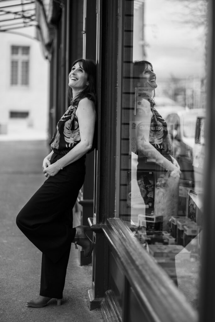 Muriel Molinier riant, appuyée contre une vitrine en ville, photo en noir et blanc