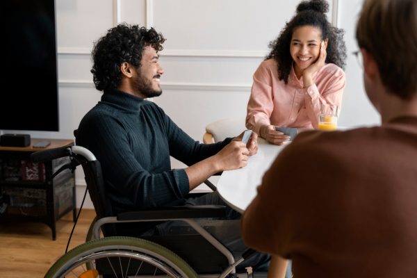 Homme en fauteuil roulant souriant, en discussion conviviale avec des collègues, illustration de l'accueil des personnes en situation de handicap