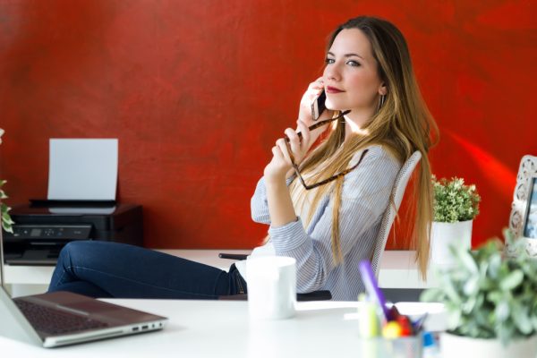 Femme souriante au téléphone dans un bureau coloré, illustrant une image professionnelle confiante